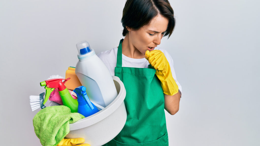 Image of lady holding cleaning supplies while coughing